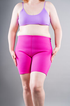 Overweight plus size woman struggling to pull up tight pink neoprene slimming shorts. Weight loss, shapewear and body shaping concept