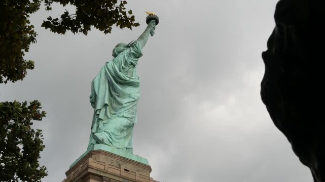 Statue of Liberty on Liberty Island, New York, United States. Cooper monument, symbol of democracy and patriotism near Manhattan, NYC USA. American independence. Autumn fall leaves. From behind, back.