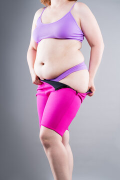 Overweight plus size woman struggling to pull up tight pink neoprene slimming shorts. Weight loss, shapewear and body shaping concept