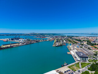 Naklejka premium Port area with ships and cranes near a city under a clear blue sky in the afternoon sunlight