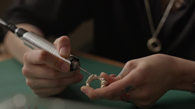 Close up of young adult Caucasian jeweler using rotary tool to polish textured silver ring at workshop workbench. Video is perfect for promoting handmade jewelry brands or craft courses