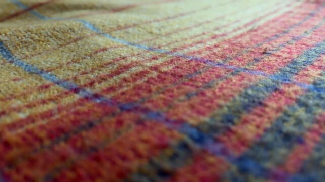 Close up slider shot revealing the intricate weave and soft texture of a colorful wool plaid tartan blanket with warm red, yellow, and blue checkered patterns