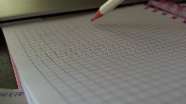 Close up of a pencil writing text on a grid paper notebook, capturing the creative process of drafting ideas, solving mathematical problems, or taking notes for study