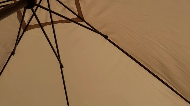 Beige patio umbrella opening slowly outdoors showcasing the mechanism and fabric canopy for sun protection on a sunny summer day, low angle point of view shot