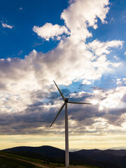 Obraz premium Wind turbine stands on a hill under a wide sky with clouds during the late afternoon