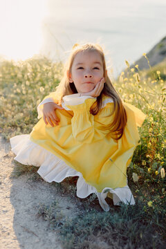 Little girl in yellow dress playing outdoors in sunny summer meadow