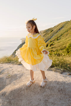 Little girl in dress standing near sea cliffs during summer day