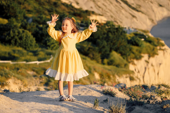 Little girl in dress standing on rocky coast with sea background
