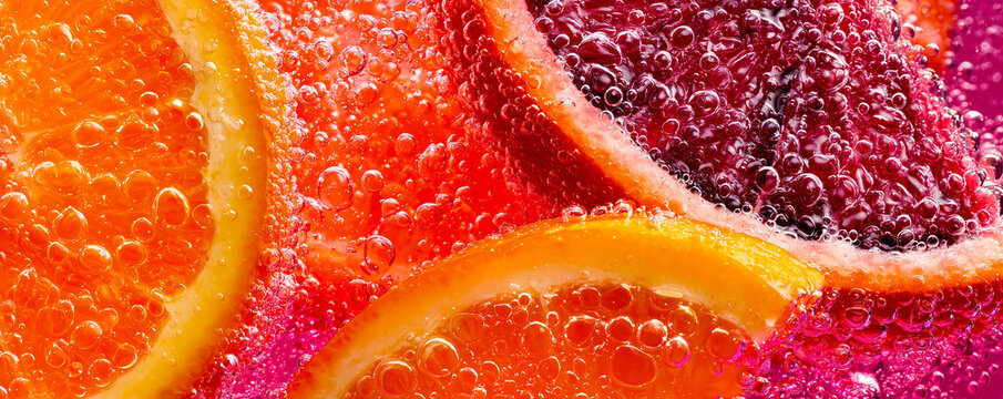 Fresh grapefruit slices submerged in sparkling water with vibrant bubbles, creating a refreshing citrus background.