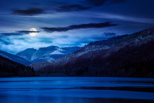 landscape with lake in autumn at night. full moon over scenic view of forest reflection on the lake surface. rika river water reserve. transcarpathia in fall season. mysterious fantasy