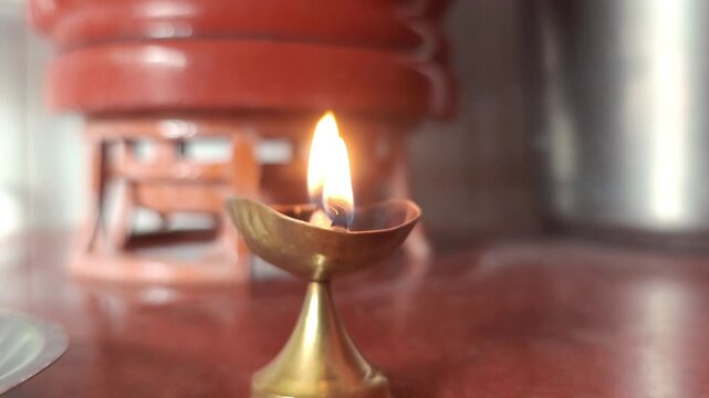 Close-up of a burning brass oil lamp diya glowing on a red floor