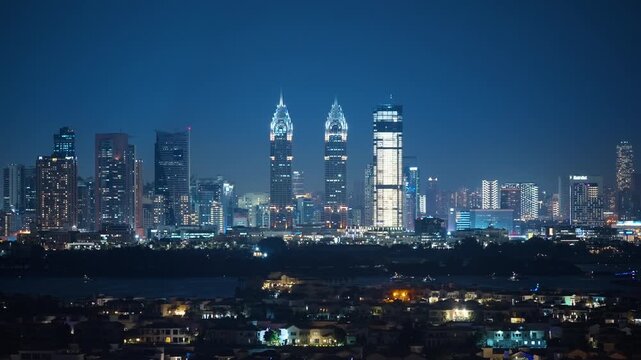 Dubai cityscape glows at night with iconic twin towers and modern skyscrapers illuminating the skyline. Residential villas in foreground contrast with towering buildings in the background.