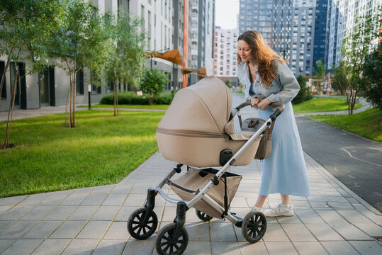 Young mother pushing a baby stroller on a paved path in a modern urban residential area, caring for her infant and enjoying an outdoor walk during daytime