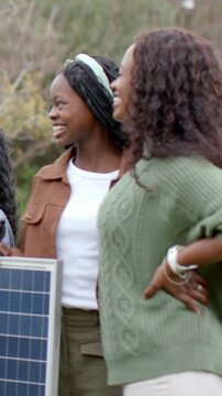 Vertical video: Smiling mother and girl holding solar panel at park after offscreen call, bracelets