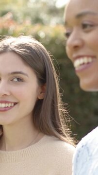 Vertical video: Turning two women leaning in park cam pulling back letting friend rest, gold hoops