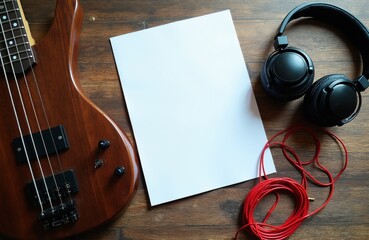 Obraz premium Bass guitar with headphones rests on wooden table near blank paper sheet for notes. Red cable coiled beside musical gear. Idea for music creation or practice setup.