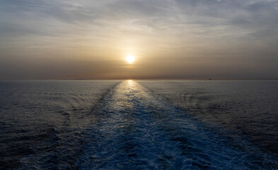 Obraz premium Sunset over calm sea with ship wake trail leading to horizon