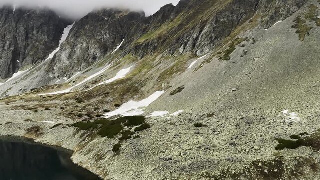 Moody Alpine Lake Tarn Surrounded by Steep Rocky Slopes and Melting Snow under Cloudy Sky: Hincovo pleso
