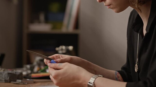 Close up of young adult Caucasian woman filing small blue polymer clay piece at workshop table. Video suitable for promoting handmade crafts, small business, or creative hobby tutorials