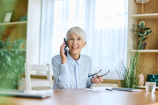 Portrait of a mature senior woman or a  businesswoman working from home having a meeting online, home office, or a student learning, or mature woman having a phone call, holding a mobile phone, smartp