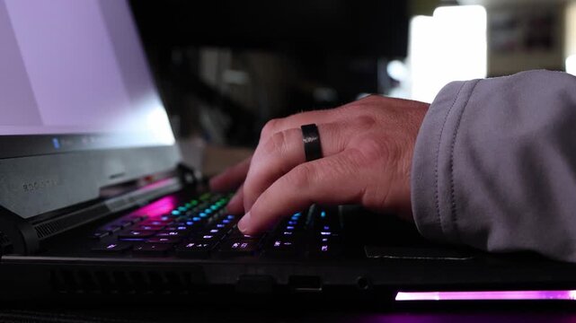 Close-up of hands typing on a gaming laptop with vibrant RGB keyboard lighting