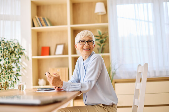Portrait of a mature senior woman or a  businesswoman working from home having a meeting online, home office, or a student learning, or mature woman having a phone call, holding a mobile phone, smartp