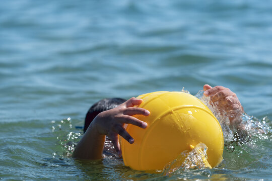 Child underwater reaching for floating buoy in open water. Dramatic concept of drowning prevention, water safety, emergency rescue, accident risk and child protection