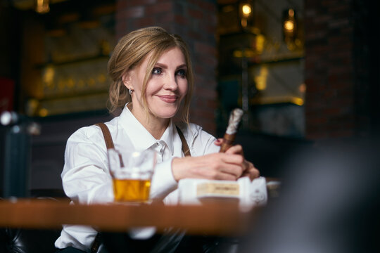 beautiful senior woman on an armchair in hat smoking cigare