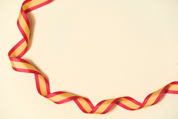 Spanish flag colored ribbon on beige background in a composition with copy space. Concept: celebration of national holidays or national achievements.