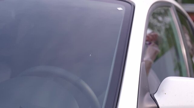 A man applies a ceramic anti-rain coating to the windows and headlights of a car.