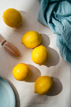 Whole lemons arranged on linen tablecloth with wooden citrus juicer in sunlight, minimalist food background