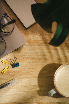 Coffee cup and laptop, with plant shadow on wooden desk, morning lifestyle background with copy space