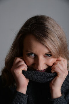 Junge Frau versteckt ihr Gesicht l&auml;chelnd im kuscheligen Strickpullover. Authentisches Lifestyle-Portrait zu Gem&uuml;tlichkeit, Hygge, W&auml;rme, Wintermode, Wohlbefinden und nat&uuml;rlicher Sch&ouml;nheit.