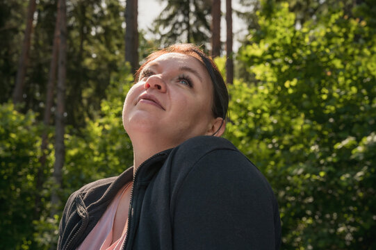 Portrait of a young woman outdoors looking upward in sunlight with a forest background