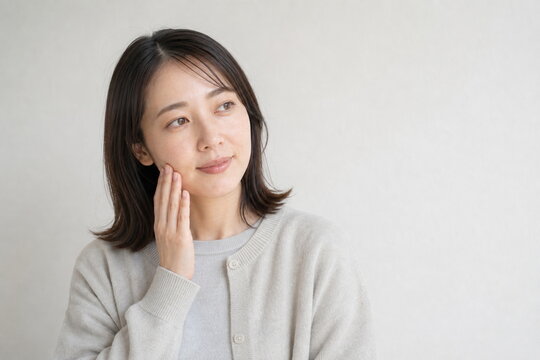 カーディガン姿で頬を触る乾燥肌ケア女性