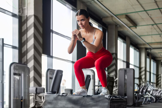 Athletic woman doing box jumping during crossfit training in modern gym.