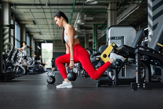 Athletic woman doing bulgarian squats with kettlebell in gym