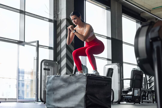 Athletic woman doing box jumping during crossfit training in modern gym.