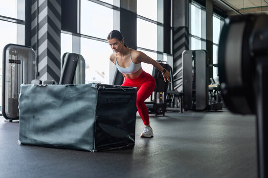 Athletic woman doing box jumping during crossfit training in modern gym.