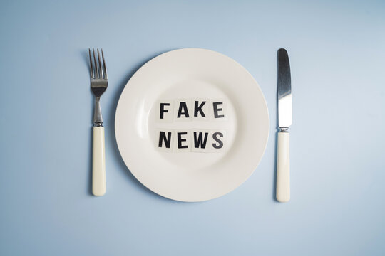 Fake news served words on plate with cutlery on blue background, misinformation and media manipulation concept