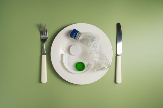Plastic bottle served on plate with cutlery on green background, plastic pollution and waste concept