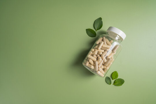 Herbal supplement capsules in bottle with leaves with green background, natural wellness concept