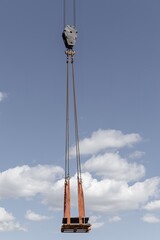 Fototapeta premium Construction site with yellow crane lifting equipment, workers in safety gear, vertical piles, and metal containers under blue sky. construction activity, heavy machinery operation, building foundatio