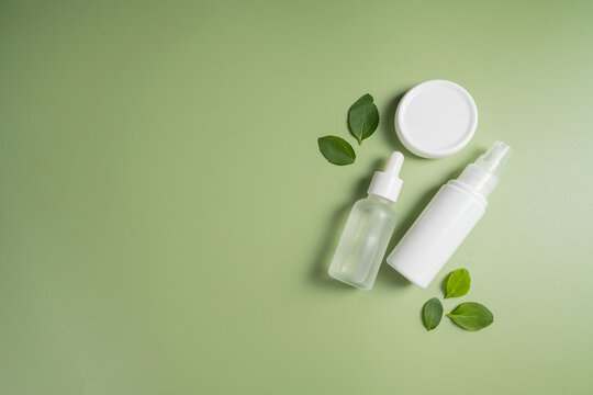 Natural skincare cosmetic containers with green leaves on pastel background, clean beauty product mockup