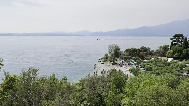Garda Lake, Bardolino, Italy. Lake beach with clear green waters and people sunbathing during summer day.