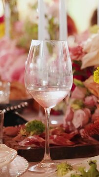Vertical video. Wine glass with drink on wedding table among flowers and table setting.