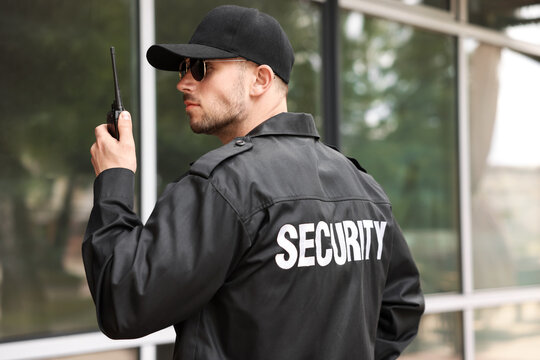 Bodyguard with earpiece using walkie talkie near building outdoors