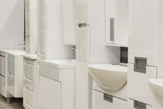 Modern bathroom furniture showroom with white vanity units, sinks and cabinets. Home improvement retail store, interior design renovation display or apartment furnishing concept.