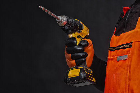 Worker hand in protective glove holding electric cordless drill or screwdriver on black background. Construction tool, building industry worker, home renovation or handyman equipment banner concept.