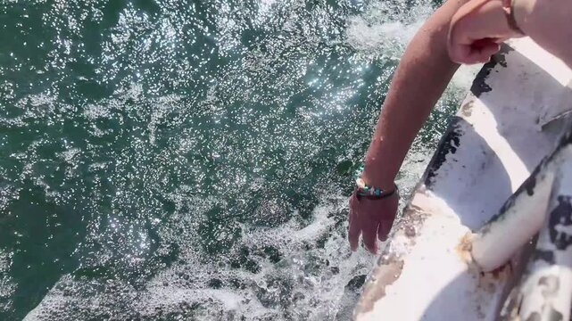 Point of view of a person's hand touching the nile river water, creating splashes and foam while sailing on a boat near philae